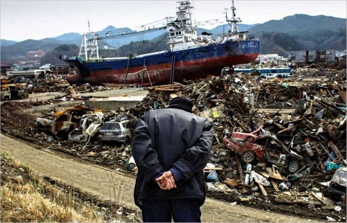Egy idős japán férfi néz le egy hegyről a szökőár sújtotta Ishinomaki városára. 2011 g